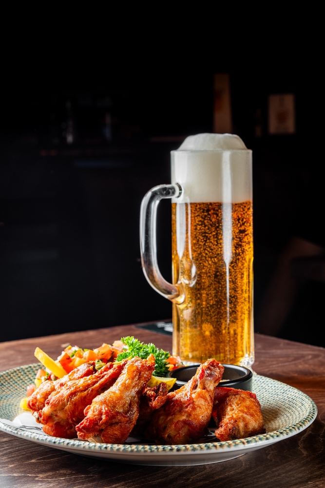 A frothy beer mug next to a plate of crispy chicken wings, fries, and vegetables on a wooden table in restaurants and bars in franklin tn, set against a dark, cozy background.